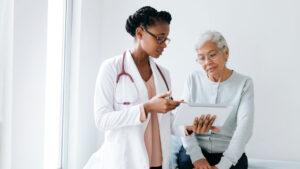 A black female doctor standing next to female patient and showing her something on digital tablet, all global, why patient research